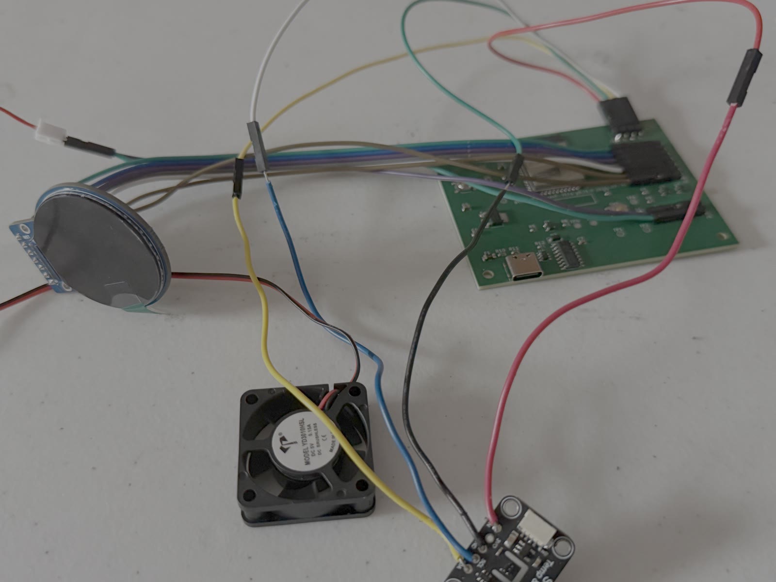 Bench bring-up: the rev E board wired to the display, fan and SHT40.