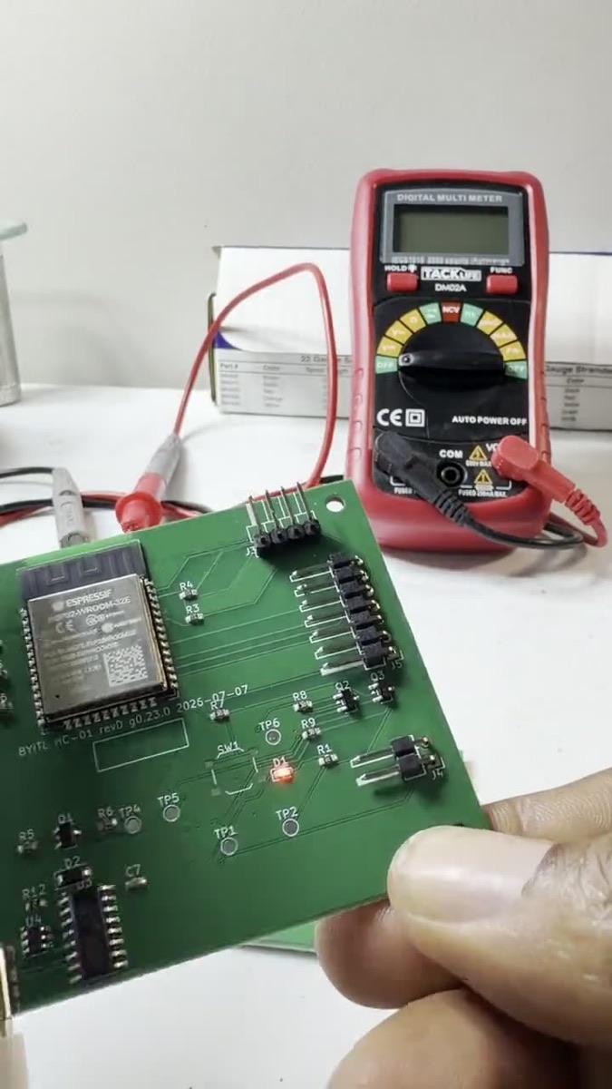 An HC-01 rev D circuit board held on the bench in front of a multimeter